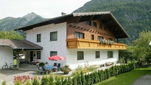 A two-story house with a balcony, a patio with outdoor seating, and a mountain backdrop. - Holiday Home in Holzgau near Snowworld Ski Area (Holzgau)