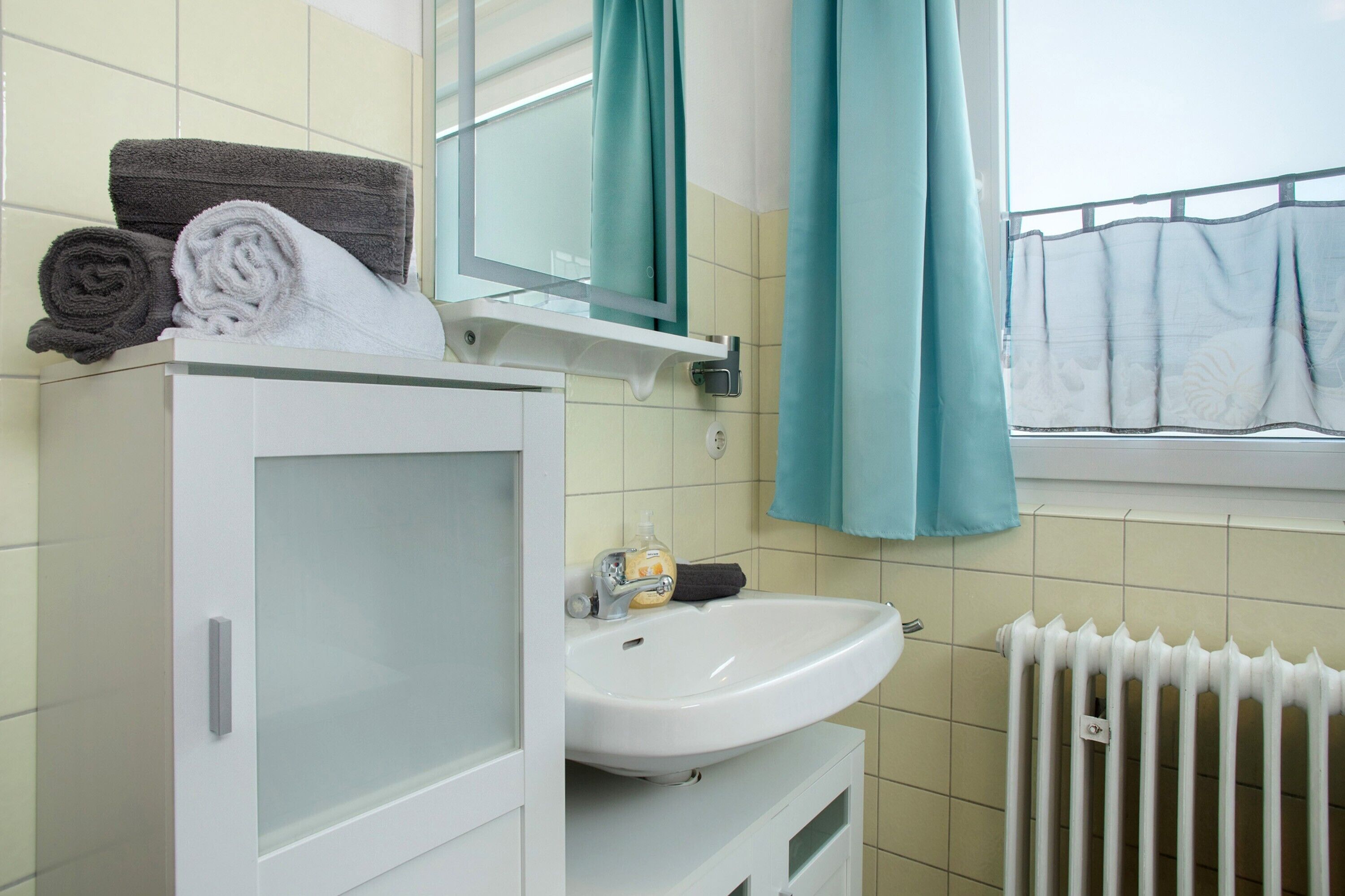 Ein Badezimmer mit einem weißen Waschbecken, einem Spiegel und einem Fenster mit Blick auf den Himmel.