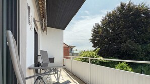 Ein Balkon mit Tisch und Stühlen, einem weißen Geländer und Blick auf Bäume und Gebäude.