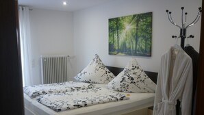 Ein Schlafzimmer mit einem Bett, einem Heizkörper, einem Waldgemälde und einem Bademantel, der an einem Haken hängt.