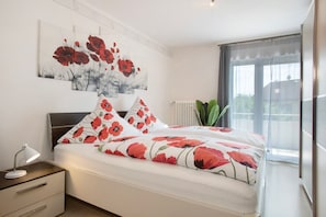 Un dormitorio con cama, mesita de noche, lámpara de pared y ventana con vistas.