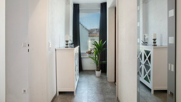 A narrow hallway with white cabinets, a potted plant, and a window with curtains.