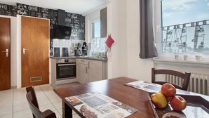 A kitchen with a coffee-themed backsplash, a dining table with apples, and a view of the sky through a window.