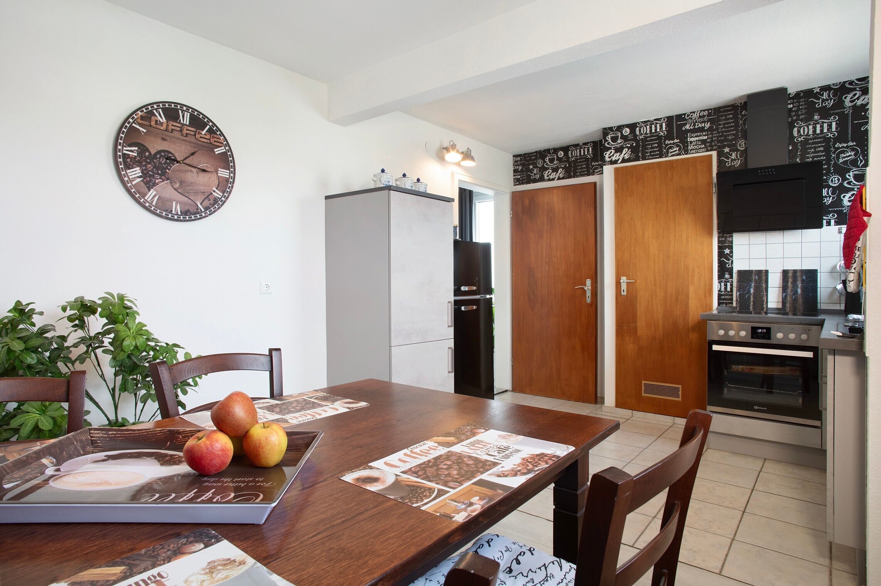 Une cuisine avec une horloge, un réfrigérateur, une porte en bois et une cuisinière.