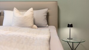 Un lit avec une tête de lit, des oreillers et une couverture. Il y a une petite table en verre avec une lampe à côté du lit.