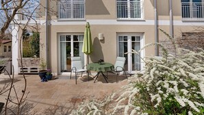 Un bâtiment doté d’un patio comprenant une table et des chaises, un banc et des plantes en pot.