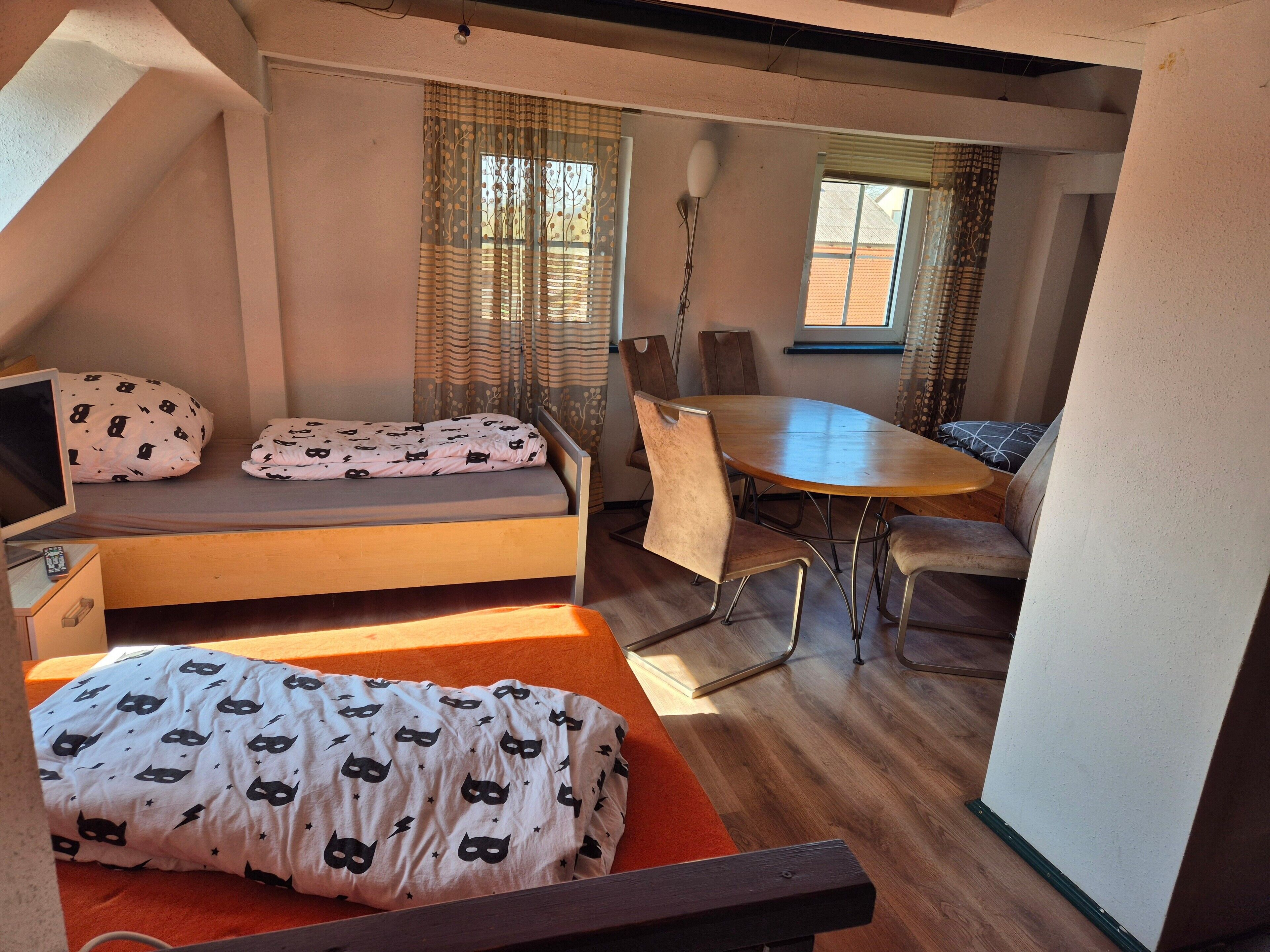 A compact room with a bed, a small table, and a chair.