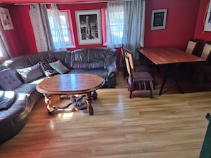 A living room with a leather sofa, a wooden coffee table, a dining table with chairs, and a window with curtains. - Country House 'Colmberg' with Shared Garden and Wi-Fi (Colmberg)