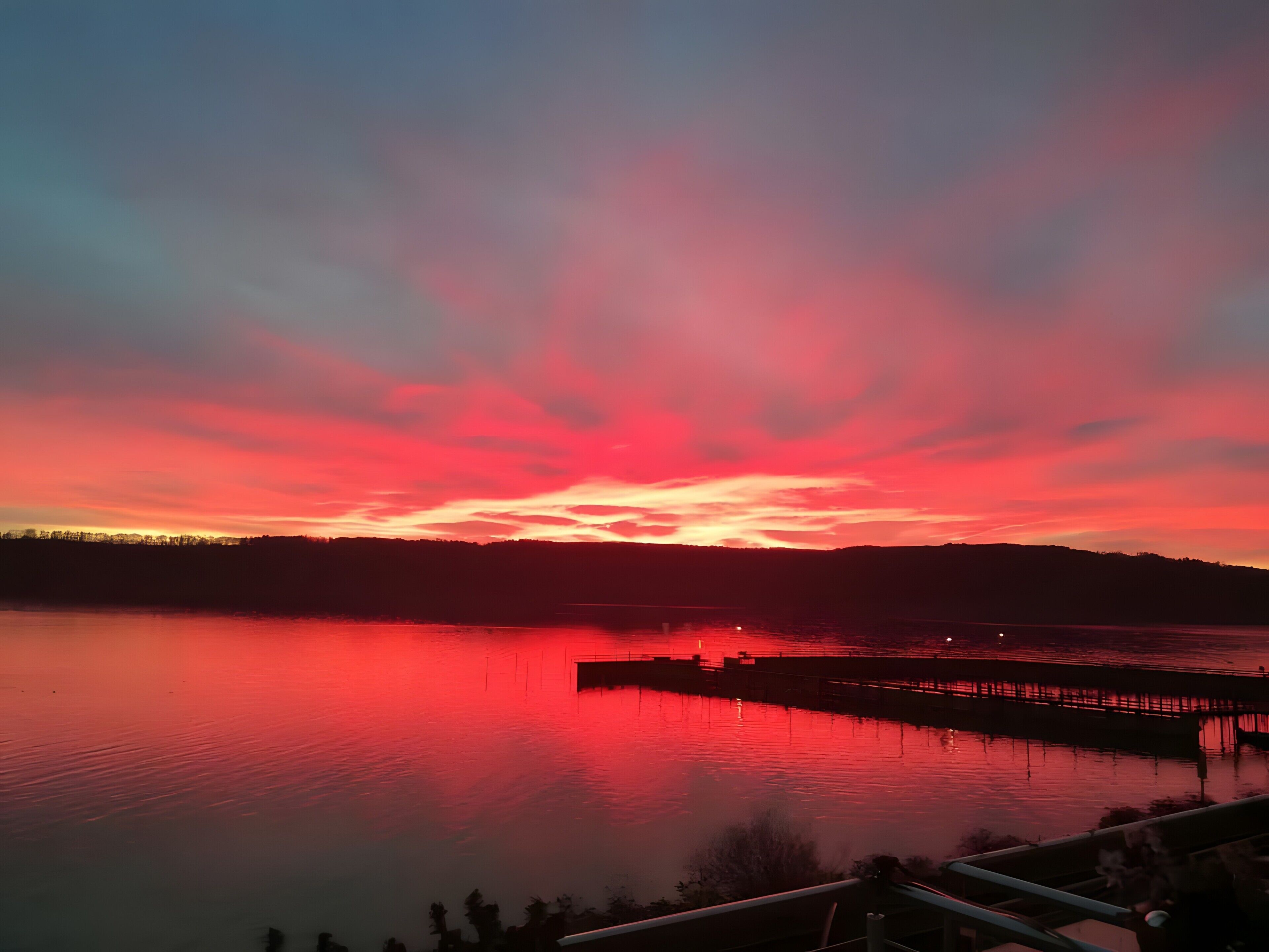 Un coucher de soleil sur un lac paisible, avec une jetée qui s’avance dans l’eau.