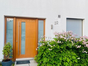 Un bâtiment moderne avec une porte en bois, le chiffre « 22 » peint sur le mur et un pot de fleurs devant l’entrée.