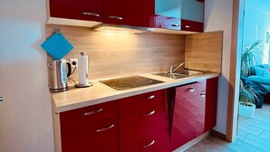 A compact kitchen with red cabinets, a stainless steel sink, and a wooden countertop. - Apartment 'Abendrot, 45qm' with Lake View, Balcony and Wi-Fi (Sipplingen)