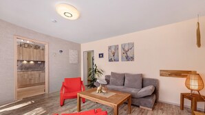 Un salón con una mesa de madera, sillas rojas, un sofá gris y obras de arte colgadas en la pared.
