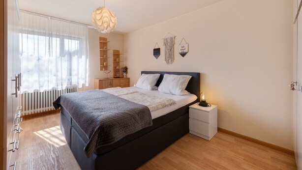 Un dormitorio con cama, mesita de noche y ventana con cortinas.