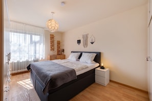 Une chambre à coucher avec un lit, une table de chevet, une commode et une fenêtre avec des rideaux.