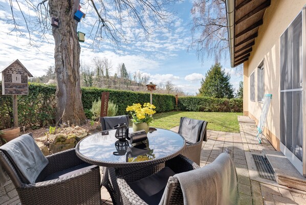 Une terrasse dotée de meubles en osier, d’une table ronde et d’un vase rempli de fleurs.