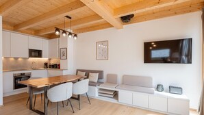 A modern kitchen with a wooden ceiling, white cabinetry, and a dining area with a wooden table and chairs.