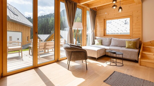 A cozy cabin with a wooden interior, large windows, a sofa, and a dining area.