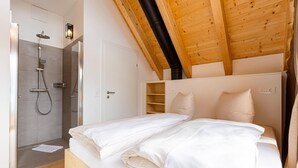 A bedroom with a wooden ceiling, a shower, and a bed with white bedding.