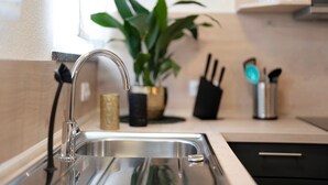 A kitchen with a stainless steel sink, a potted plant, and kitchen utensils on the counter.