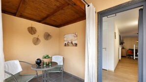 A small patio with a table and chairs, a ceiling with exposed beams, a wall with decorative leaves, and a door leading to an interior space.