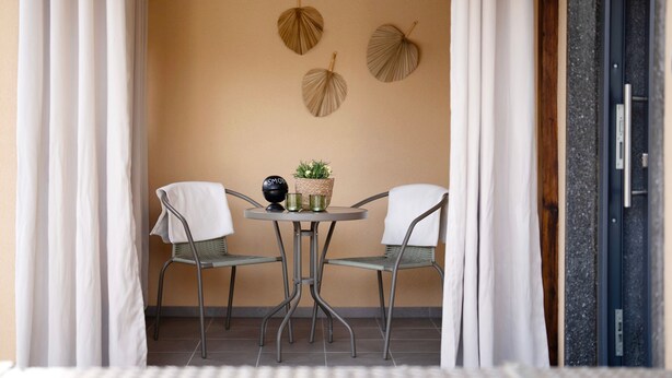 A small patio with a round table and two chairs, a basket with plants, and decorative leaves on the wall.
