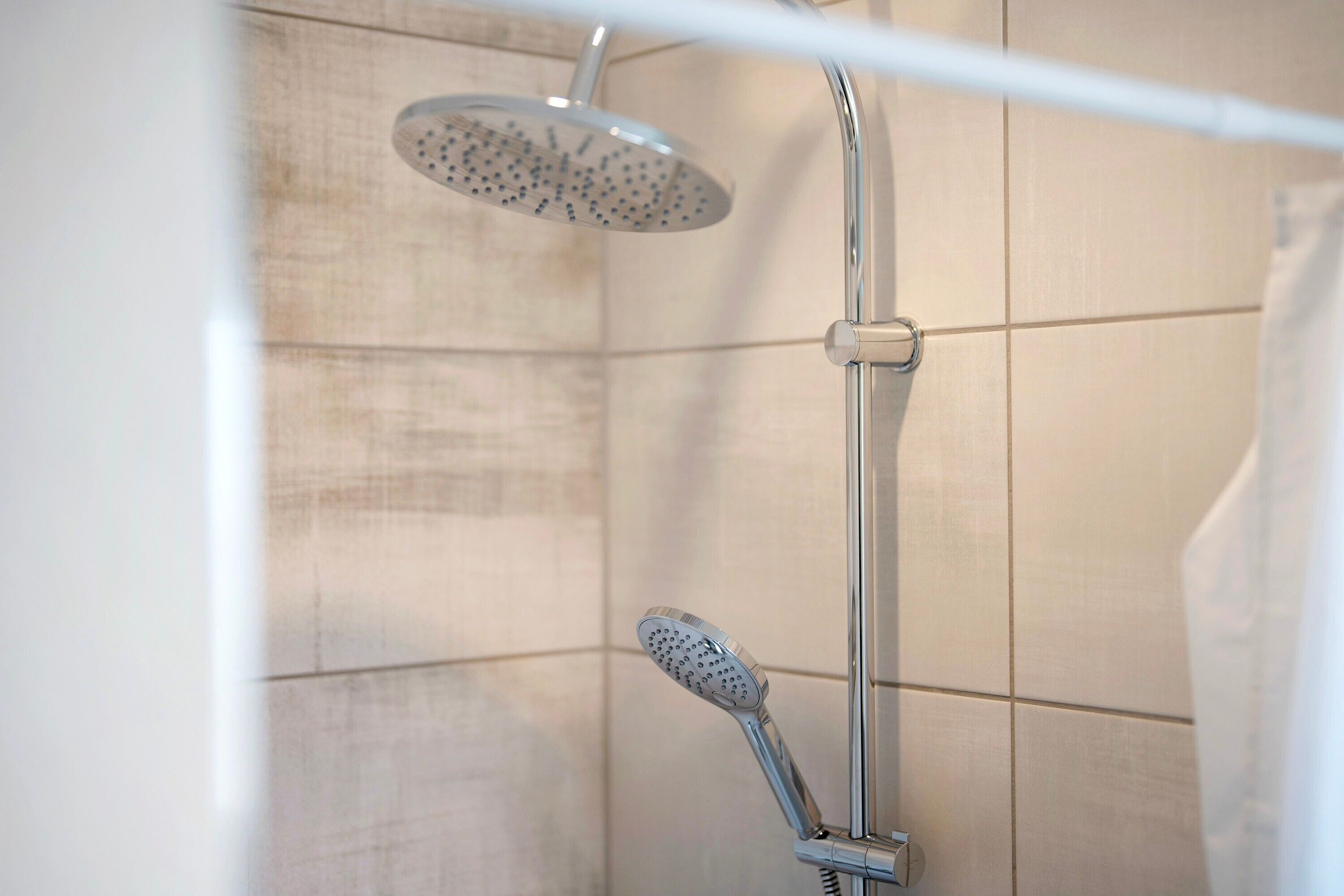 Une douche équipée d’un pommeau de douche à main et d’un pommeau de douche fixe au plafond, dans une salle de bain carrelée.