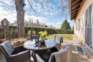 An outdoor patio with wicker furniture, a round glass table, and a potted plant.