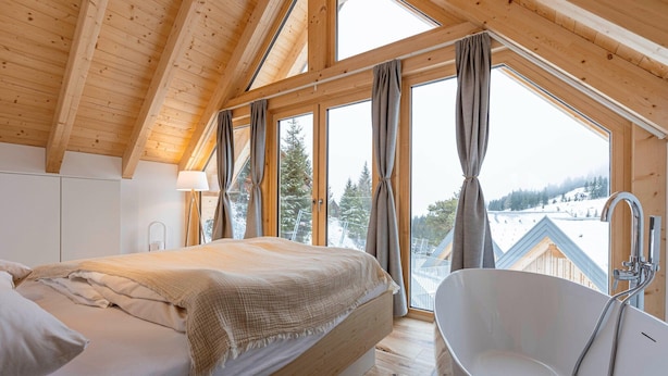 Quarto com uma cama grande, uma banheira e vista para uma paisagem nevada através de amplas janelas.