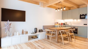 Uma cozinha moderna com piso de madeira, uma mesa de jantar com cadeiras, forno embutido e uma grande TV de tela plana fixada na parede.
