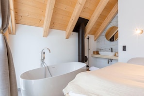 A modern bathroom with a freestanding bathtub, wooden ceiling beams, a marble wall, and a built-in sink. - Cosy chalet with sauna (Lachtal)