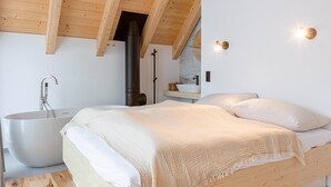 Quarto com uma cama grande, uma banheira branca e teto de madeira.