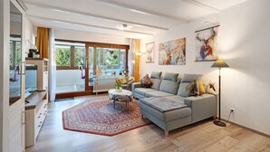 Un salon moderne avec un canapé, une table basse et une lampe sur pied. Il y a une grande fenêtre avec des rideaux, des œuvres d’art accrochées aux murs et un radiateur.