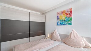 Une chambre à coucher comprenant un lit, une table de chevet, un tableau abstrait aux couleurs vives et une armoire.