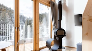 A modern room with a large sliding glass door leading to a balcony, a black heater, and a round table with chairs.