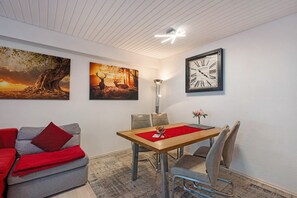 A dining area with a wooden table, grey sofa, and red throw pillows. - Apartment '101 Luisa' with Mountain View, Balcony and Wi-Fi (Schönwald im Schwarzwald)
