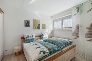 A bedroom with a bed, a small stool, a window with curtains, and wall art. - Apartment '101 Luisa' with Mountain View, Balcony and Wi-Fi (Schönwald im Schwarzwald)