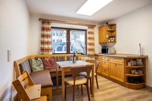 Une cuisine compacte avec un coin repas, des meubles en bois et une fenêtre avec des rideaux.