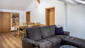 Un salon moderne avec un canapé gris, une table à manger en bois, des chaises et un plafond avec des poutres apparentes.
