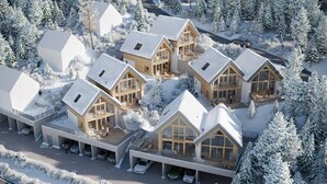 A modern lodge with multiple wooden cabins, a covered parking area, and a snowy forest backdrop. - Chalet in Lachtal with sauna (Lachtal)