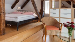 Une chambre avec un plafond en bois, un lit avec un cadre en métal, une chaise en osier, une commode et un vase rempli de fleurs.