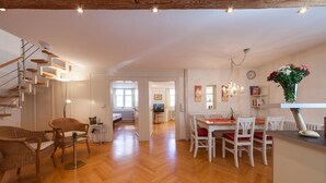 Un intérieur moderne avec un plancher en bois, un coin repas avec des chaises blanches, un escalier avec des rampes en bois et un lustre.