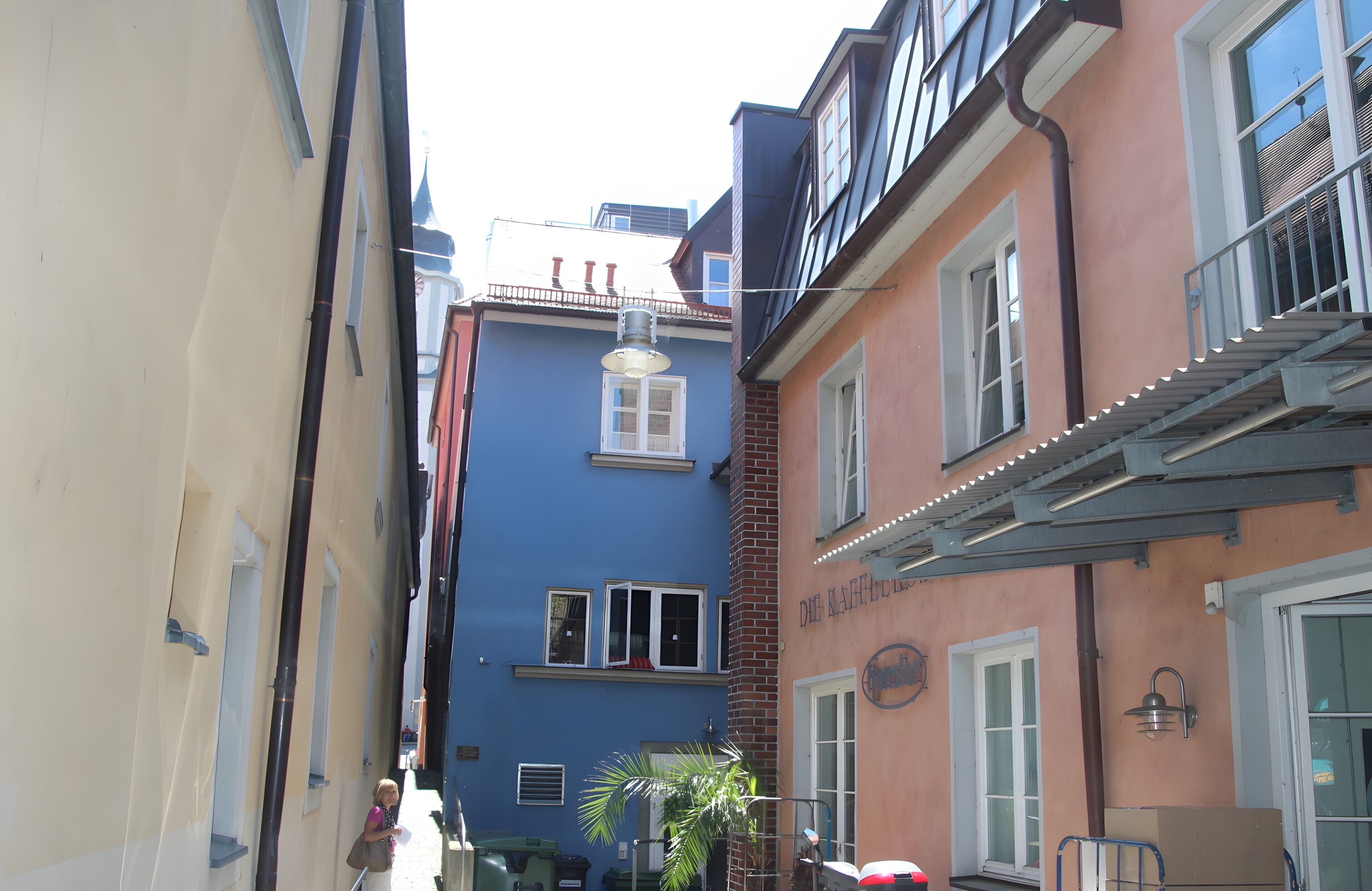 Een smalle straat met gebouwen, waaronder een blauw gebouw met een raam en een deur, en een roze gebouw met een balkon.