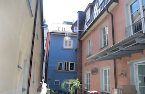 Una calle estrecha con edificios, incluyendo un edificio azul con ventana y puerta, y un edificio rosa con balcón.