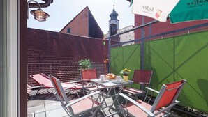 Une terrasse extérieure avec des chaises et une table en métal, un mur végétal et, au fond, un bâtiment avec un toit rouge.