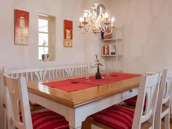 Un espace repas comprenant une table en bois, des chaises blanches, un lustre et des éléments décoratifs muraux.