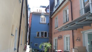 A narrow street with buildings, including a blue building with a window and a door, and a pink building with a balcony. - Apartment 'Kaufmannshaus' with Wi-Fi (Lindau am Bodensee)