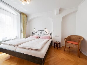 A bedroom with a bed, a chair, a small table, and a window with curtains. - Apartment 'Kaufmannshaus' with Wi-Fi (Lindau am Bodensee)