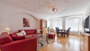 A modern living room with a red sofa, a glass coffee table, a dining area with a table and chairs, and a television on a wooden cabinet. - Apartment 'Kaufmannshaus' with Wi-Fi (Lindau am Bodensee)