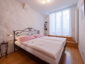 Quarto com cama, luminária de cabeceira e janela com cortinas.