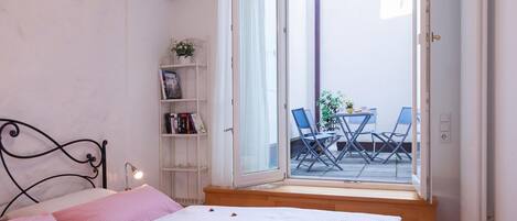 Un dormitorio con cama, una estantería y vistas a un patio exterior con mesa y sillas.